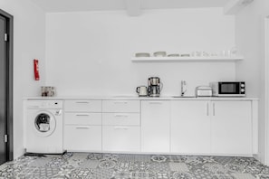 A compact kitchen with a washing machine, a coffee maker, and a microwave.