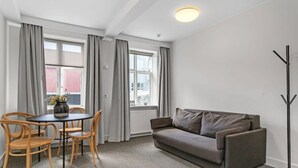 A modern living room with a grey sofa, wooden chairs, a small round table with a vase, and a floor lamp. - Superior Apartment Su (Reykjavík)