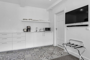 A modern kitchen with white cabinets, a coffee maker, a microwave, and a flat-screen TV mounted on the wall.