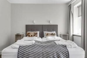A neatly made bed with a patterned blanket, two bedside tables with lamps, and a window with curtains.