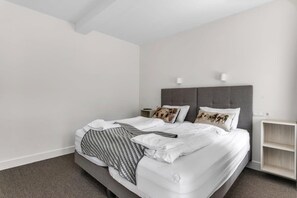 A modern hotel room with a large bed, a bedside table, a nightstand, and a wall-mounted light fixture.