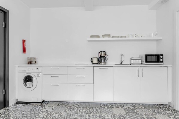 A compact kitchen with a washing machine, a coffee maker, and a microwave.