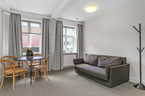 A modern living room with a grey sofa, wooden chairs, a small round table with a vase, and a floor lamp.