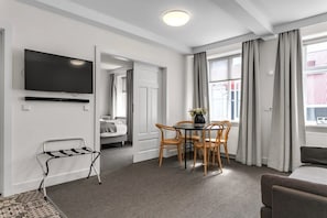 Una habitación de hotel moderna con televisión de pantalla plana, una zona de comedor con mesa y sillas, un sofá y vistas al exterior.
