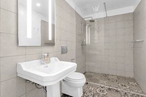 A modern bathroom with a white sink, toilet, and shower. The walls are tiled with a light color, and there's a patterned floor.