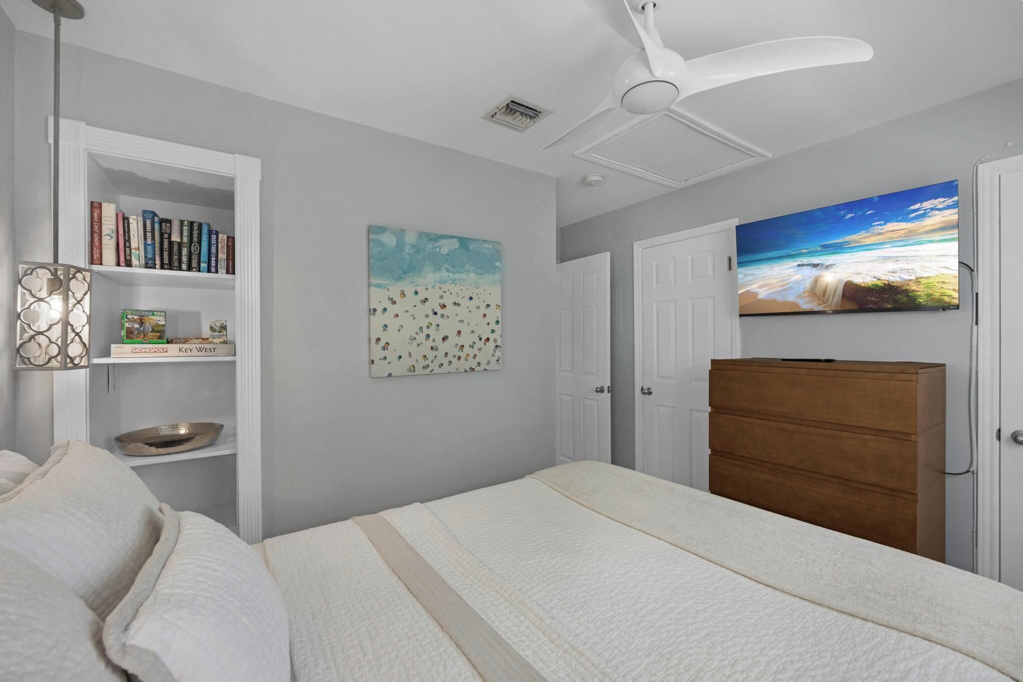 A bedroom with a bed, a bookshelf, a painting, a dresser, and a ceiling fan.