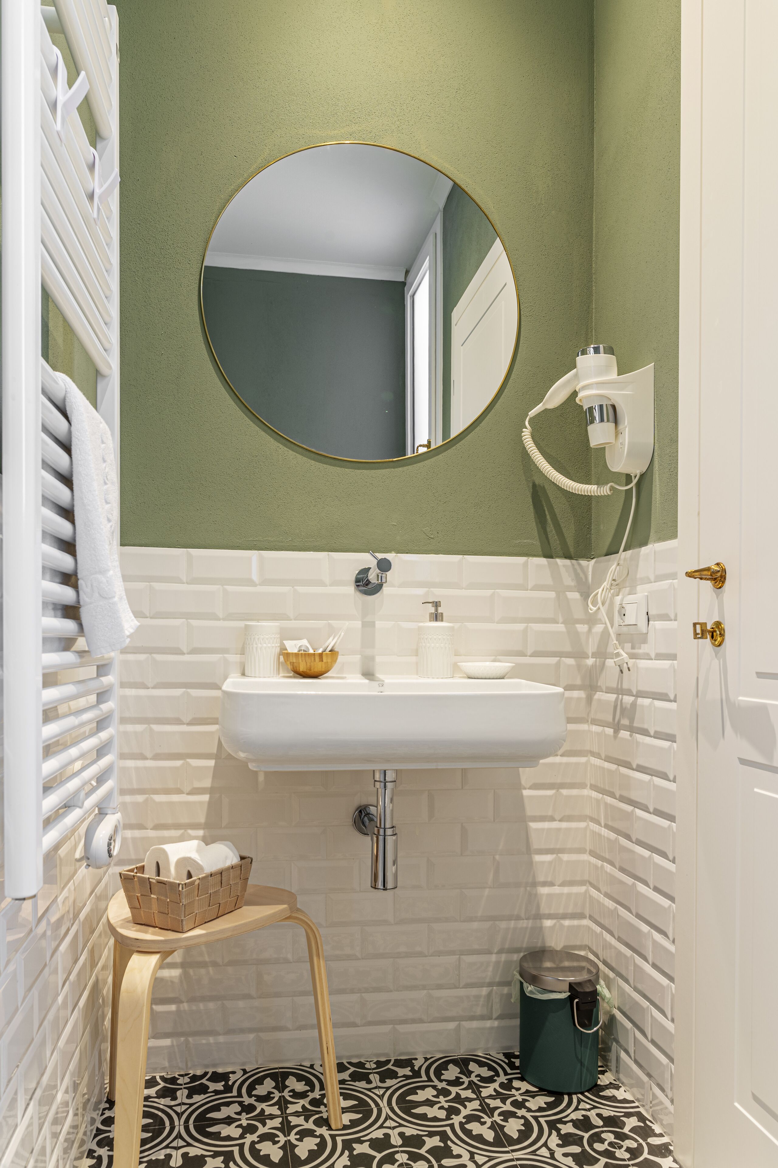 Un baño con un lavamanos blanco, paredes verdes, un espejo redondo y un suelo estampado.