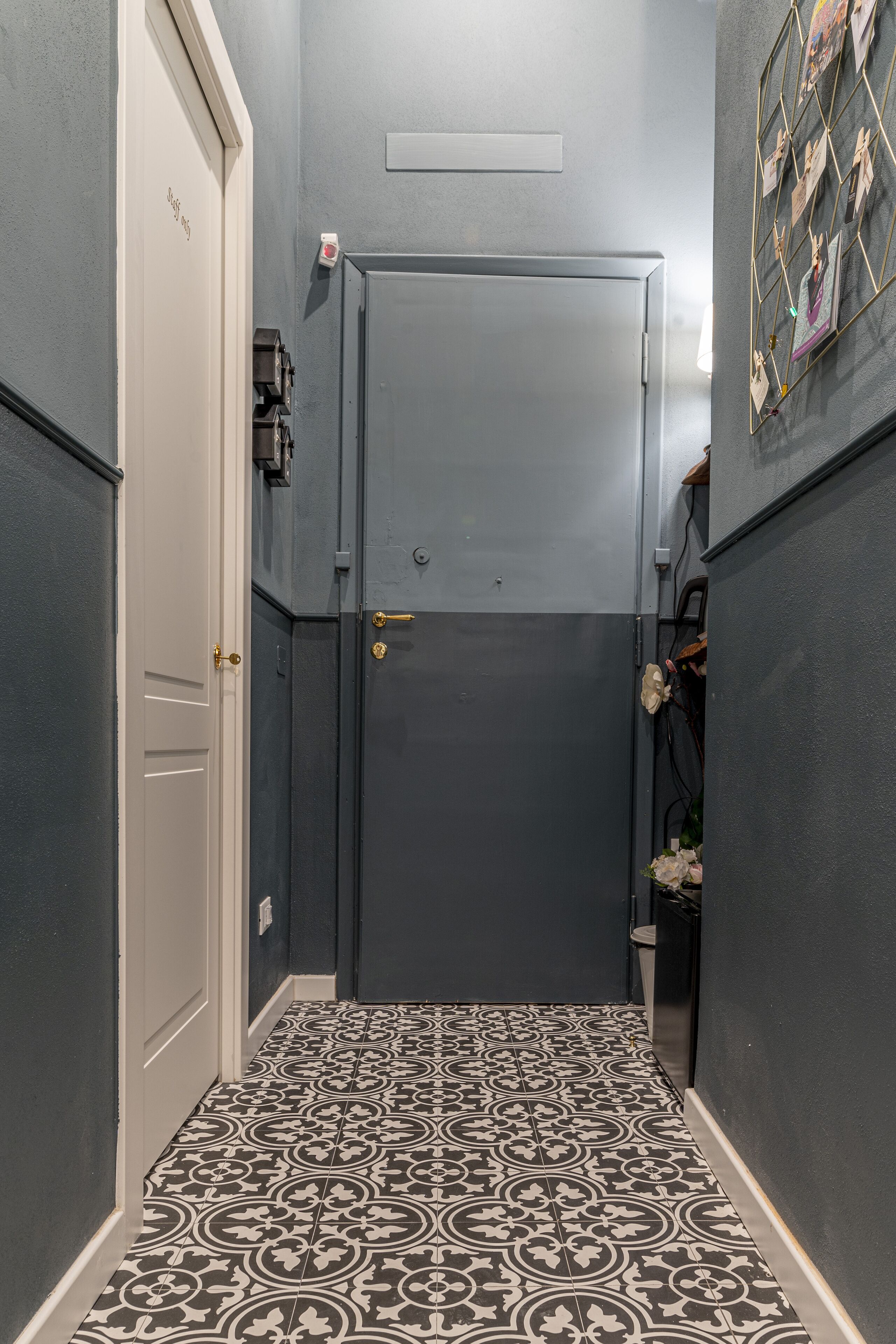 A narrow hallway with patterned floor tiles, a door with a brass handle, and a wall-mounted photo frame.