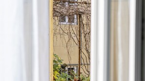 A view through a window of a building with a yellow exterior, a balcony with plants, and a stone railing. - La Lu Cozy Rooms 2 (Pisa)