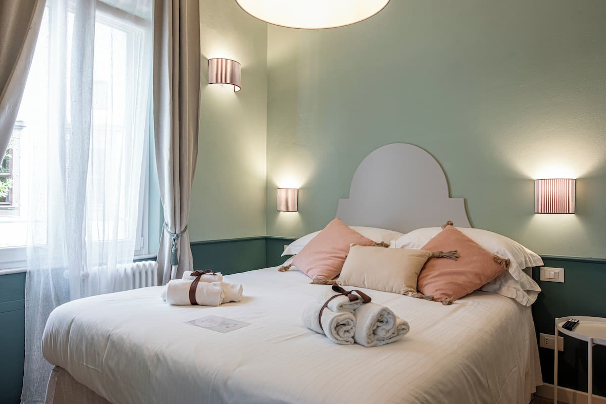 A neatly made bed with rolled towels and pillows, a bedside table with a remote control, and wall-mounted lamps.