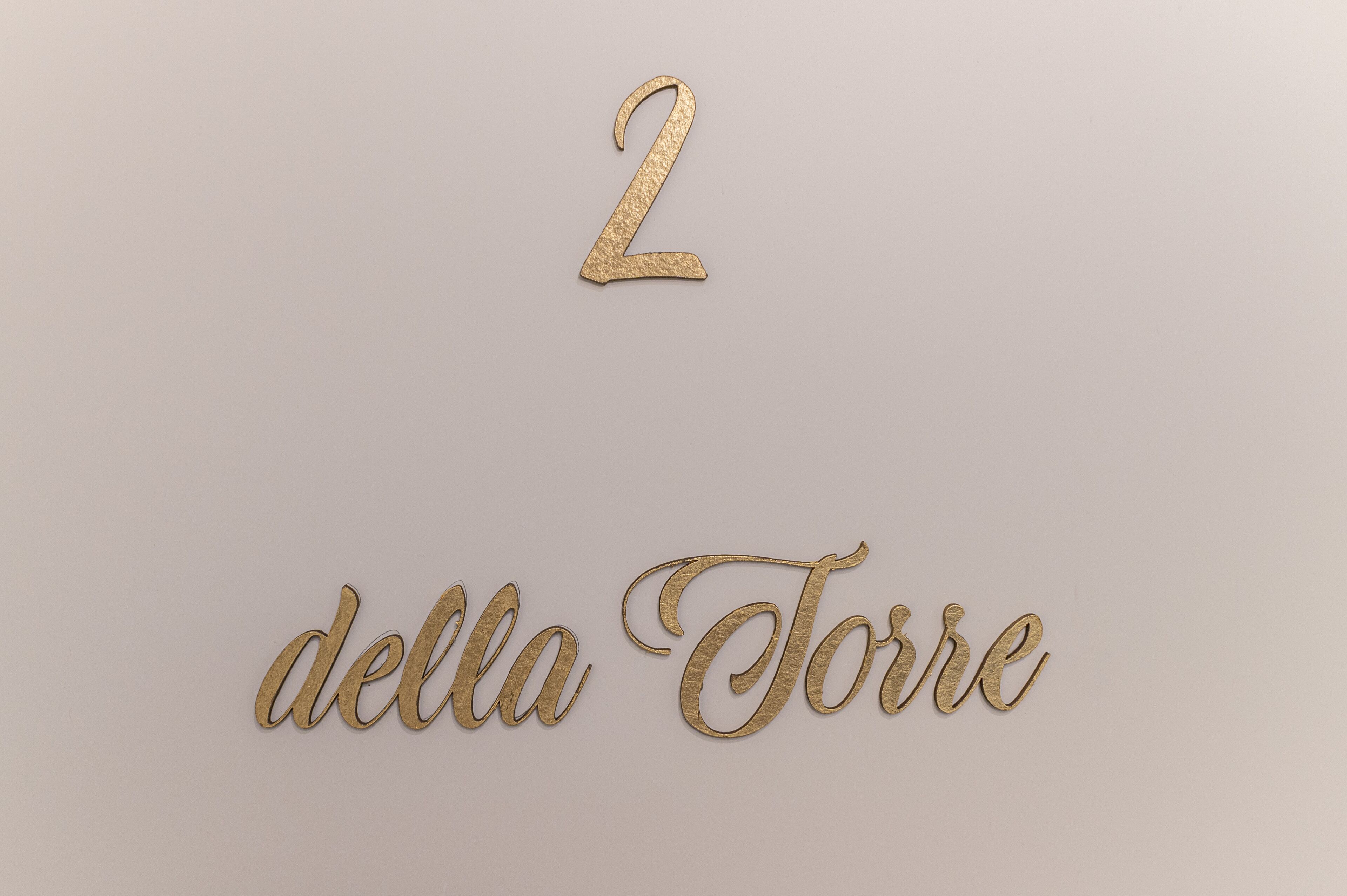 Um número '2' dourado decorativo e a inscrição 'della Torre' sobre um fundo liso.