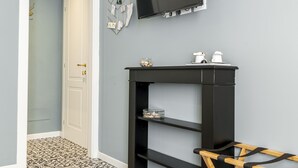 A room with a grey wall, a mounted TV, a black shelf with decorative items, patterned floor tiles, and a door leading to another room. - La Lu Cozy Rooms 2 (Pisa)