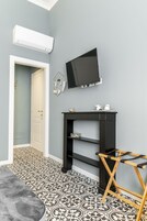 Una habitación con pared gris, un televisor montado, un estante negro con adornos y un suelo de baldosas estampadas, además de una puerta que da a otra habitación.
