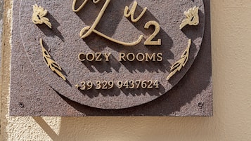 A metal plaque with the text "B&B La Lu 2 COZY ROOMS" and a phone number, mounted on a wall with a keypad below it.