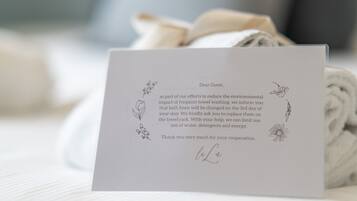 Une carte de remerciement posée sur un lit, à côté d’une serviette enroulée.
