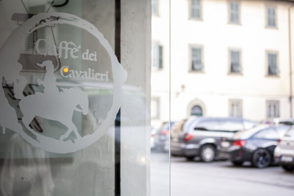 A window with a decorative sign reading "Caffè dei Cavalieri" and a blurred view of parked cars outside. - La Lu Cozy Rooms 2 (Pisa)