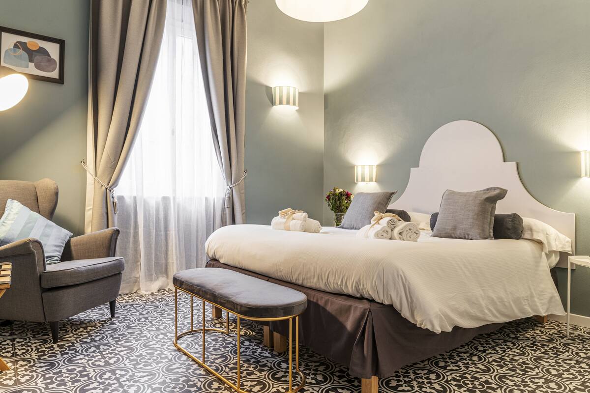 A bedroom with a bed, a chair, a bench, and a nightstand.