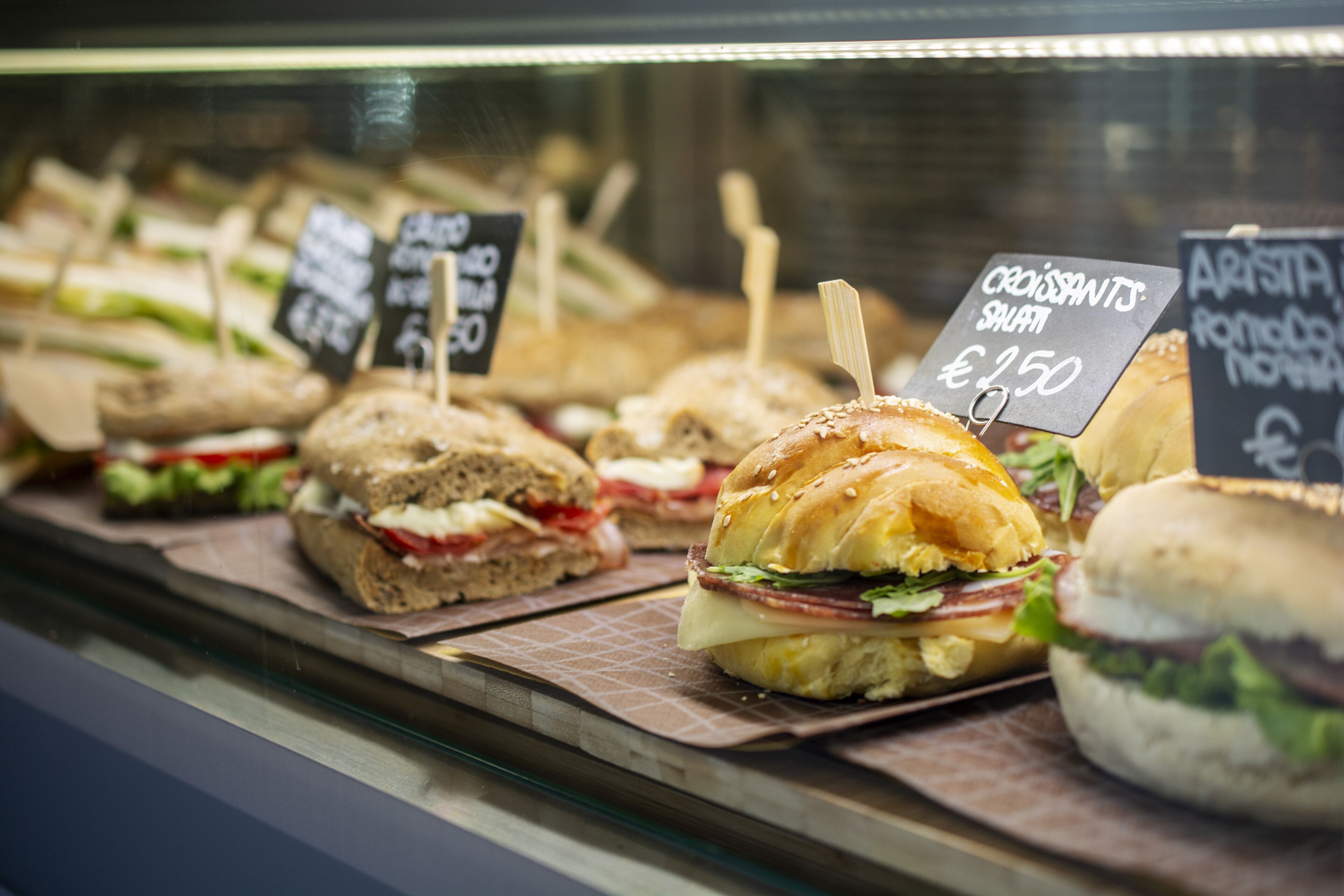 Una vitrina con varios sándwiches y pasteles, cada uno con su etiqueta de precio.