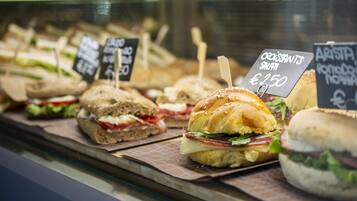 Una vitrina con varios sándwiches y pasteles, cada uno con su etiqueta de precio.