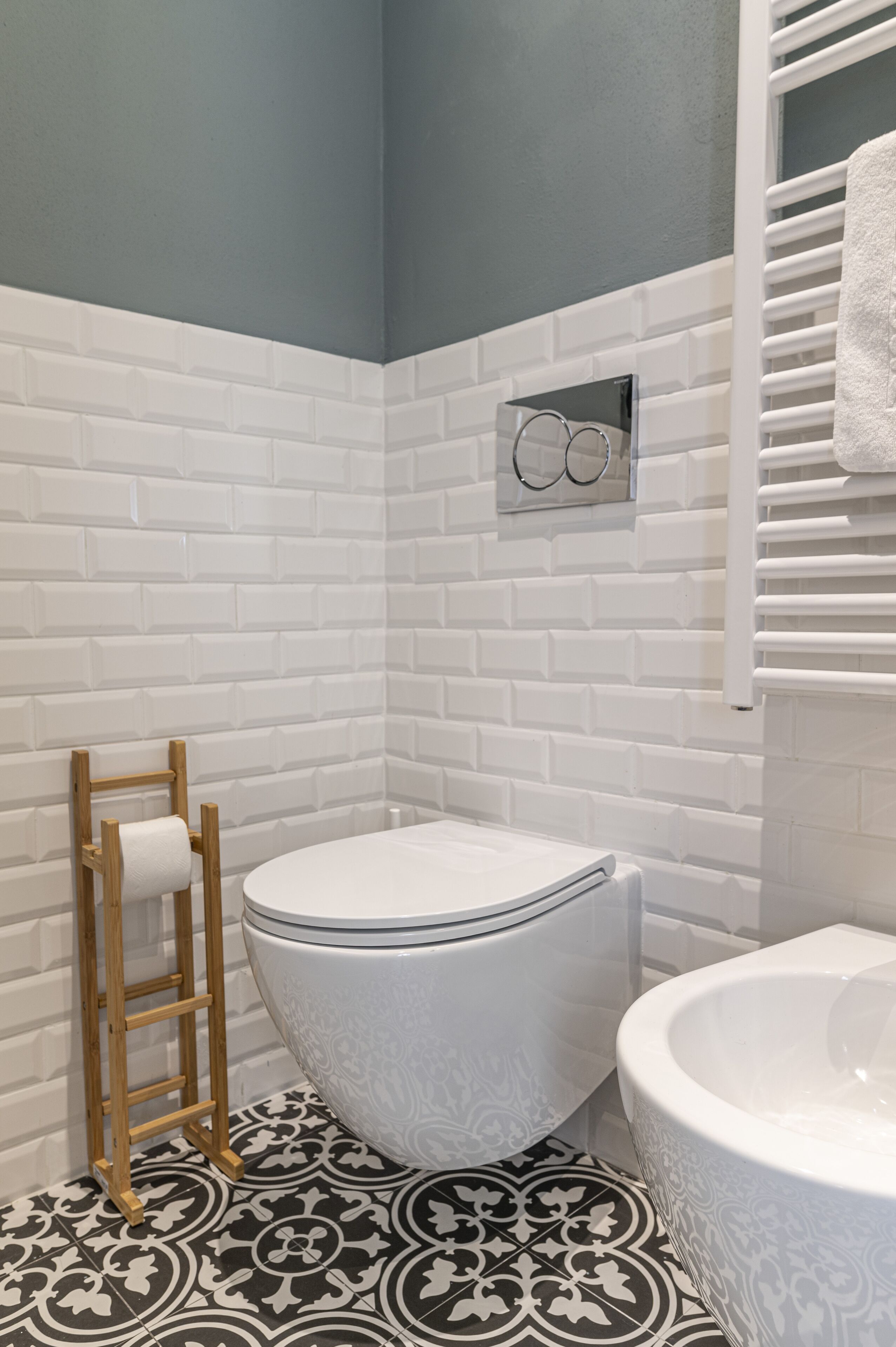 Une salle de bain avec des carreaux de céramique blancs rectangulaires, un carrelage décoratif au sol, des toilettes, une baignoire et un porte-serviettes.
