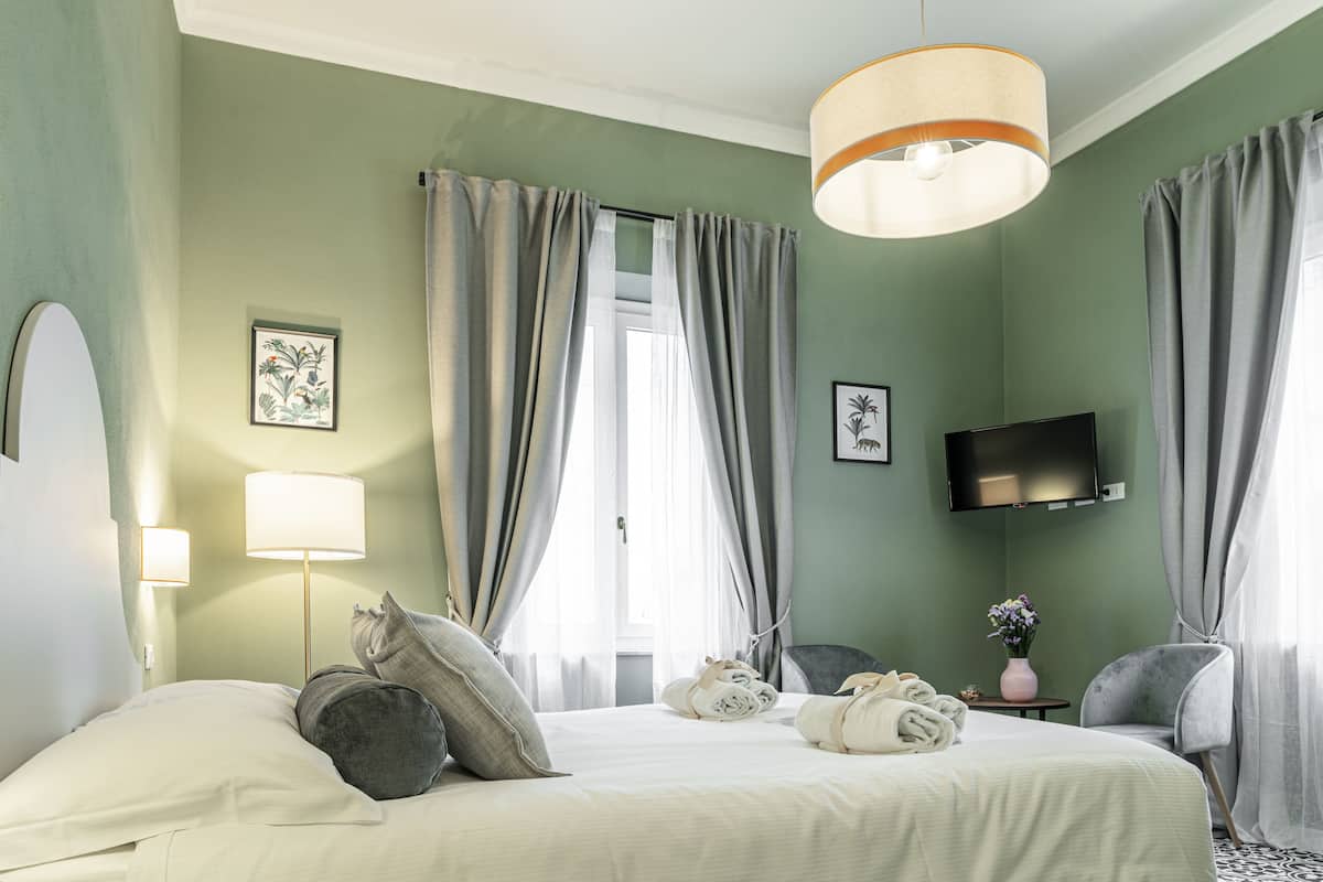 A hotel room with a bed, a TV, a chair, a lamp, and a window with curtains.