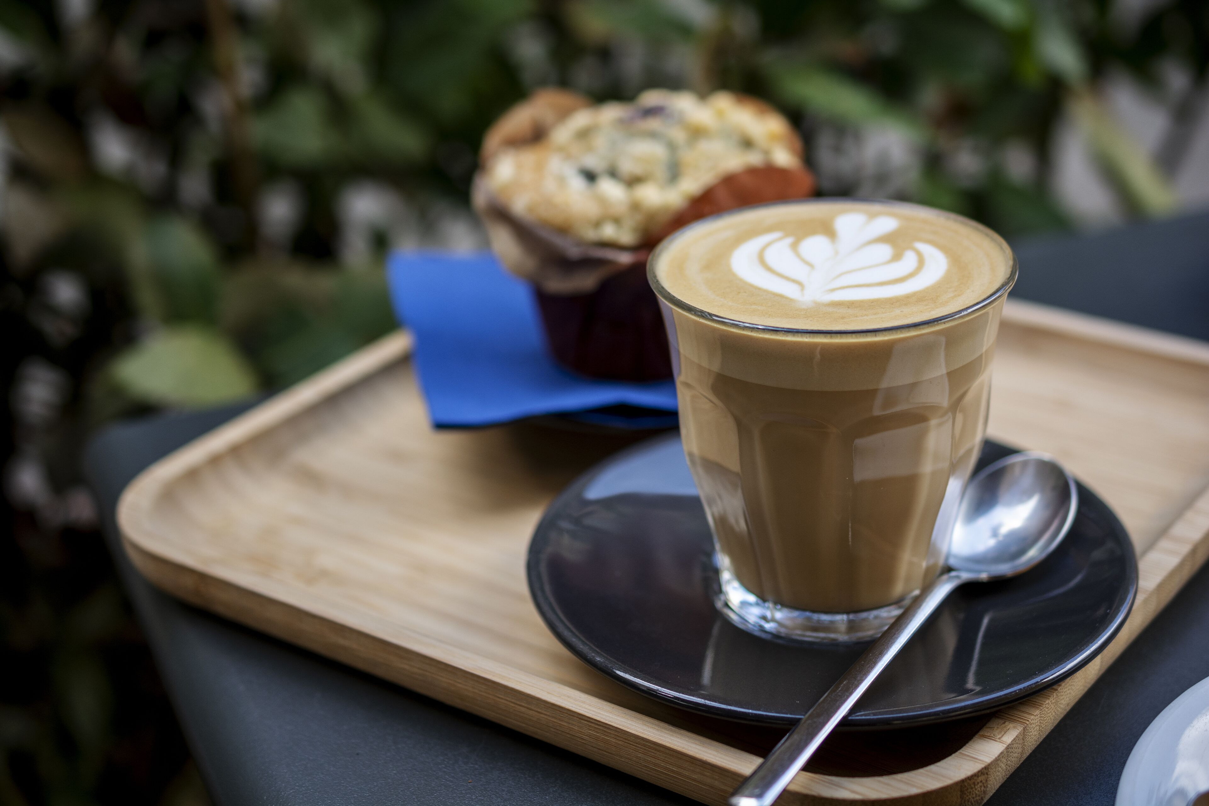 Een kop koffie met latte-art op een houten dienblad, samen met een muffin en een lepel.