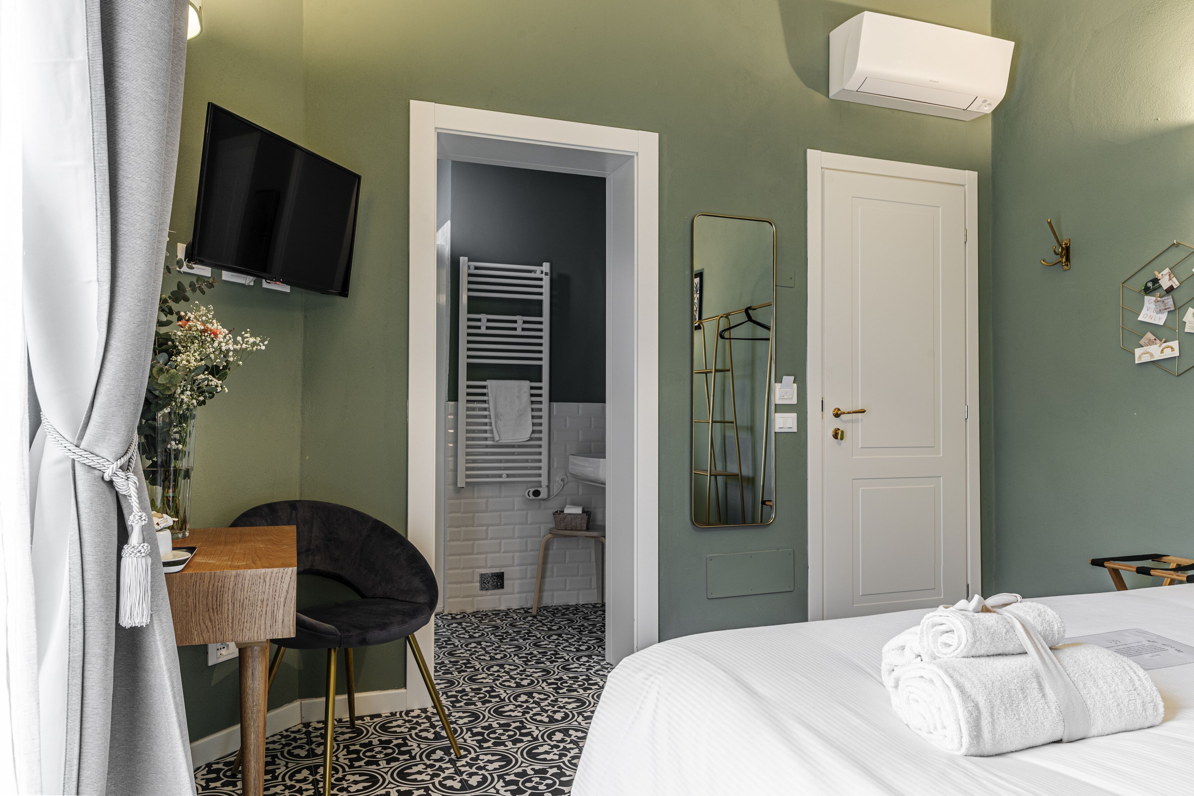 A hotel room with a bed, a TV mounted on the wall, a mirror, and a door leading to a bathroom.