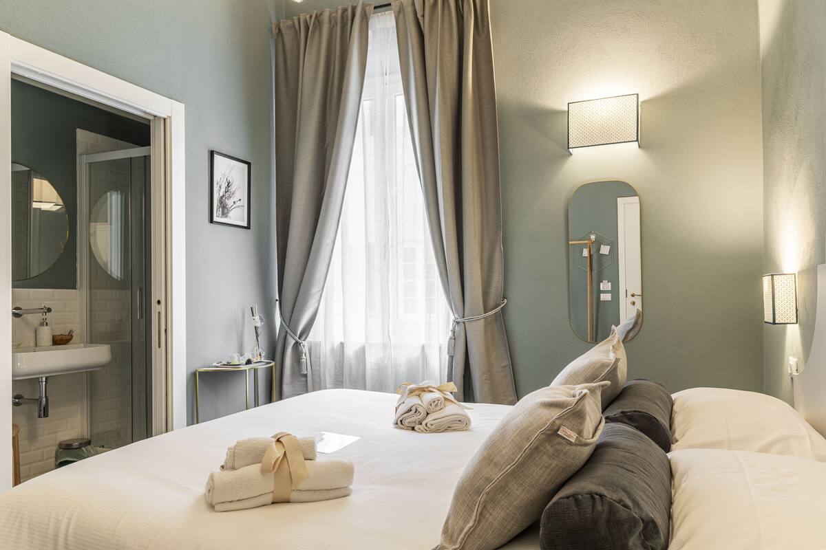 A hotel room with a bed, a bathroom with a sink, a mirror, and a window with curtains.