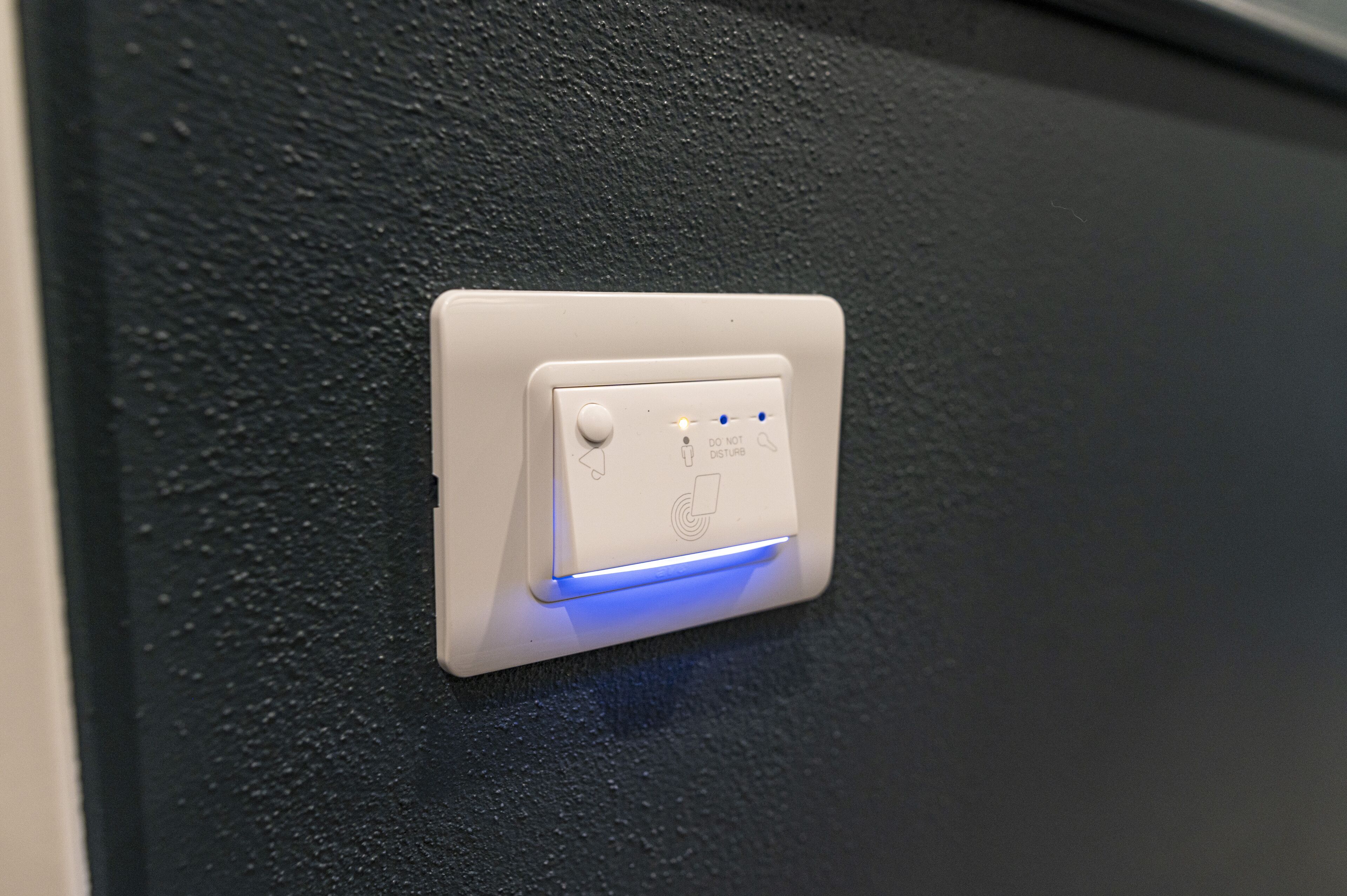 A white switch with a blue light indicator on a textured black wall.