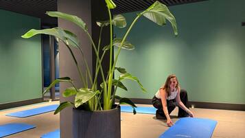 Un estudio de yoga con una planta grande en maceta, colchonetas de yoga azules y una persona practicando.