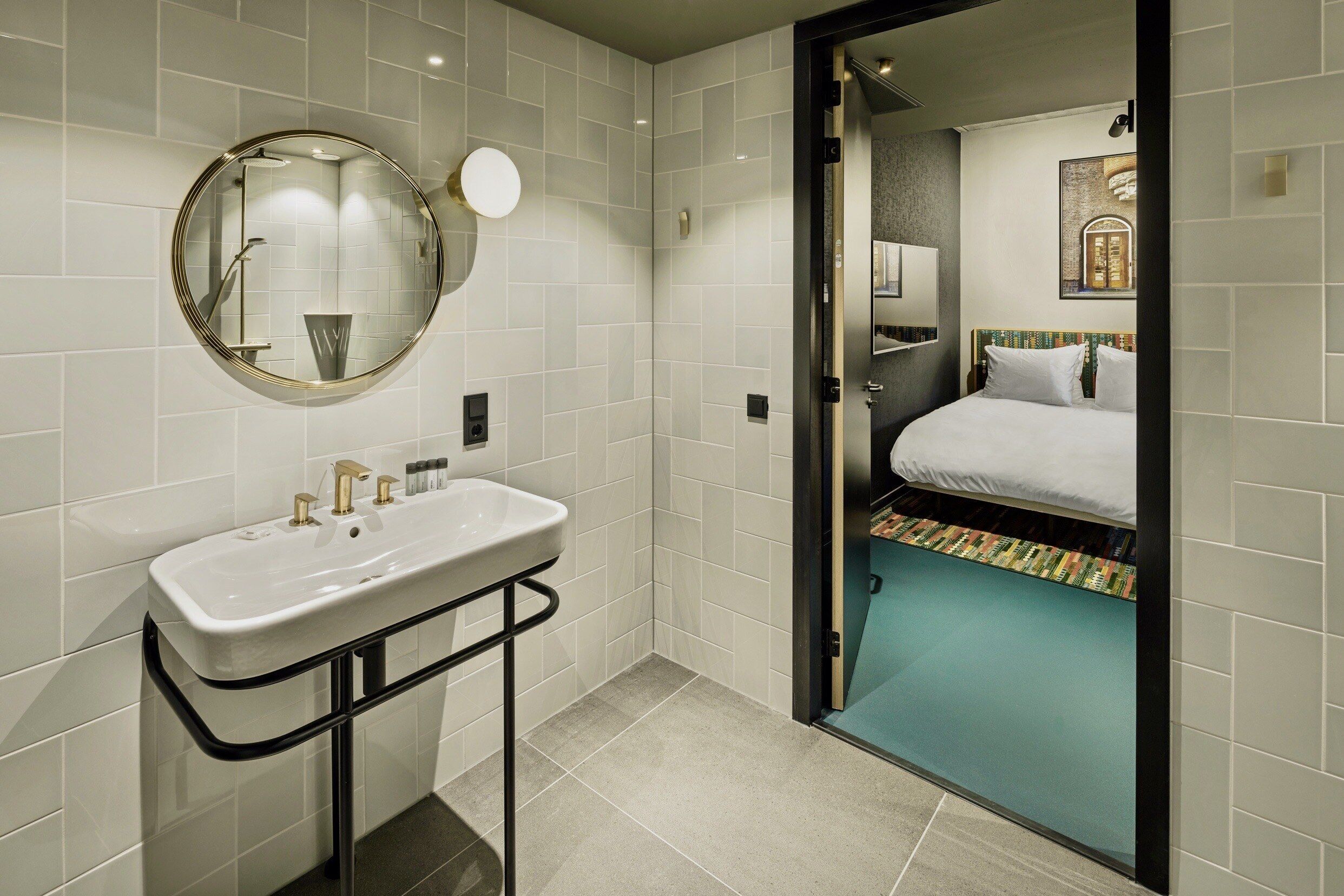 Un baño moderno con un lavamanos blanco, un espejo redondo y una ducha.
