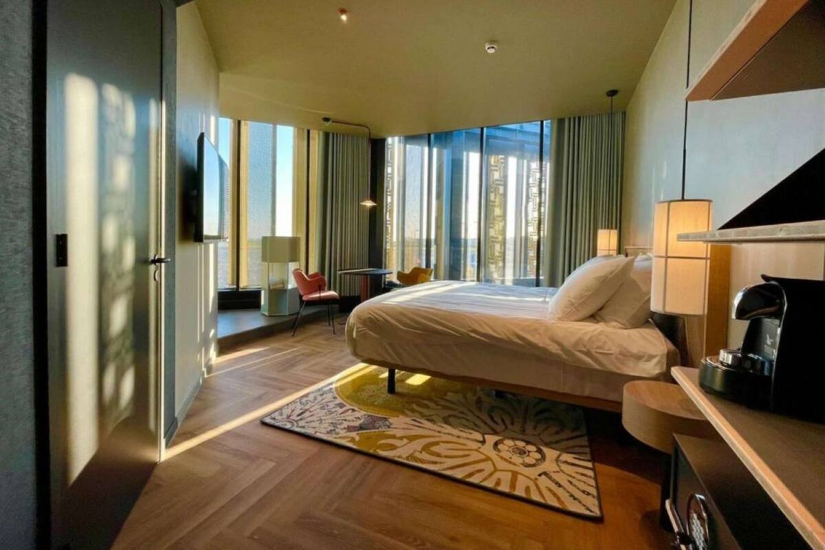 A modern hotel room with a large bed, a desk, a chair, and a TV.