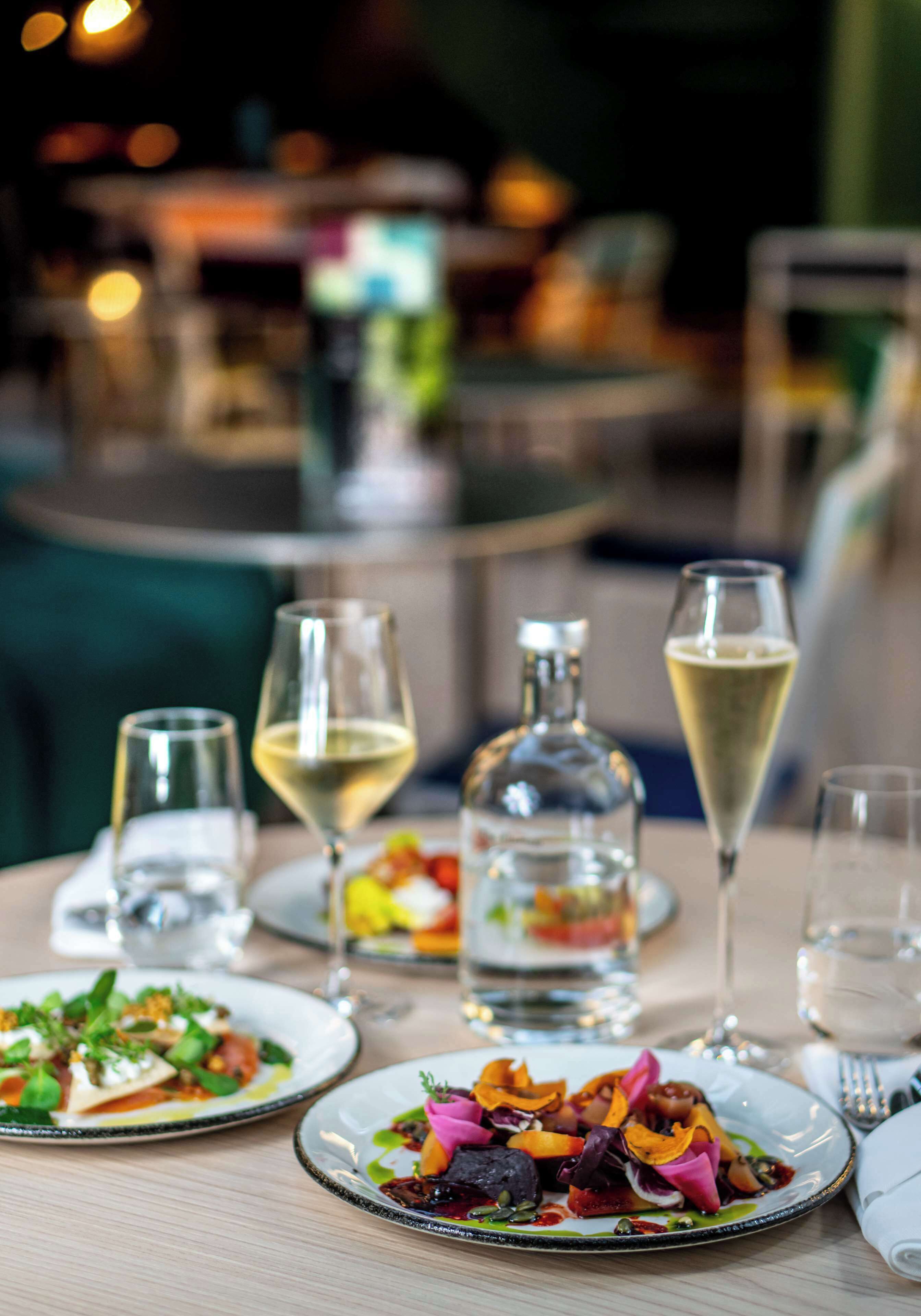 A dining table with plates of food, glasses, and a bottle.