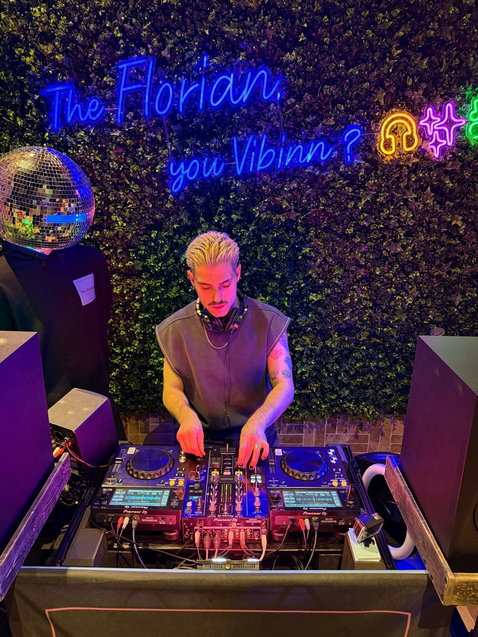 A DJ booth with Pioneer DJ equipment, a disco ball, and a neon sign reading "The Florian, you Vibe?"