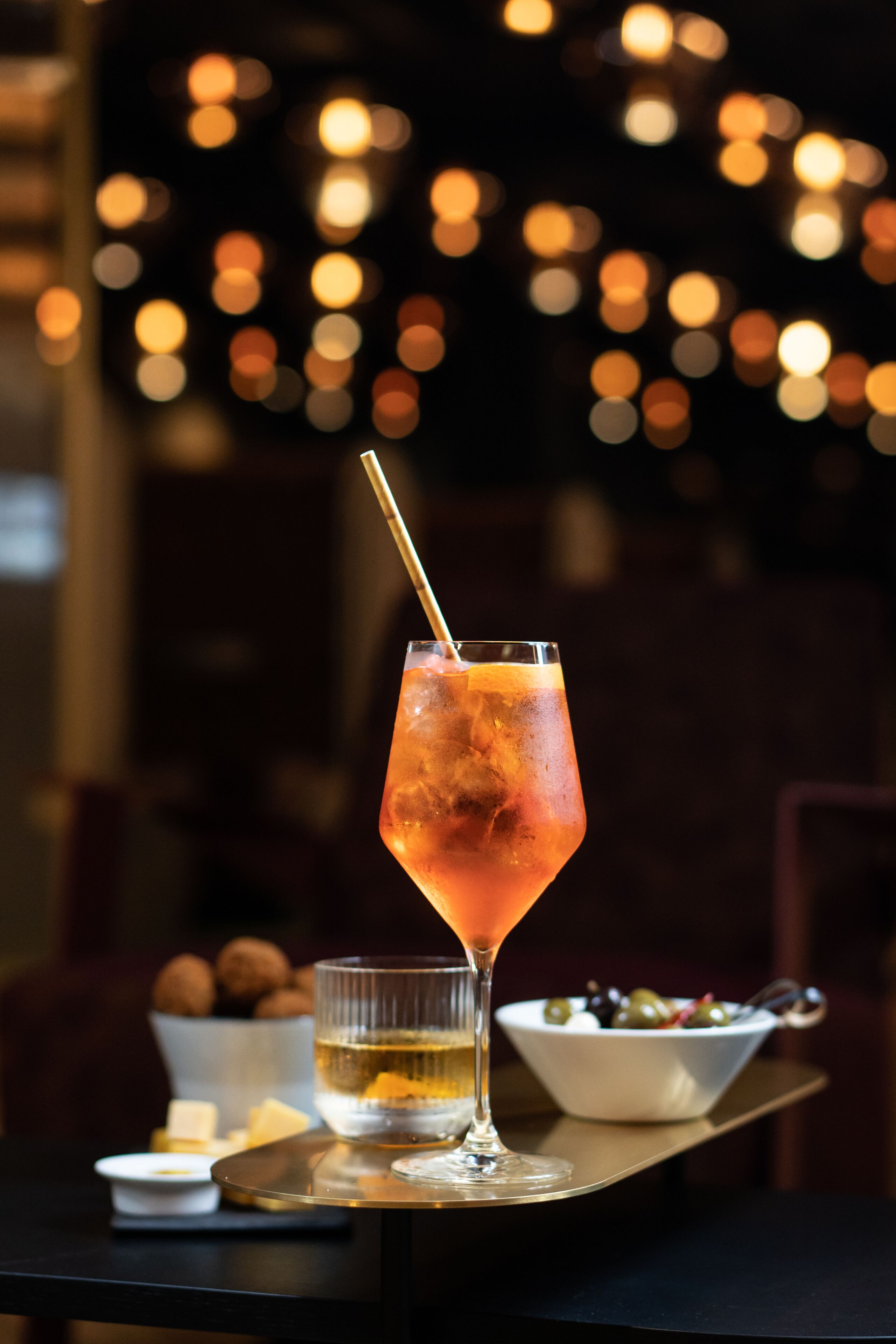 A cocktail glass with a straw on a tray, a small bowl of olives, and a container of butter.