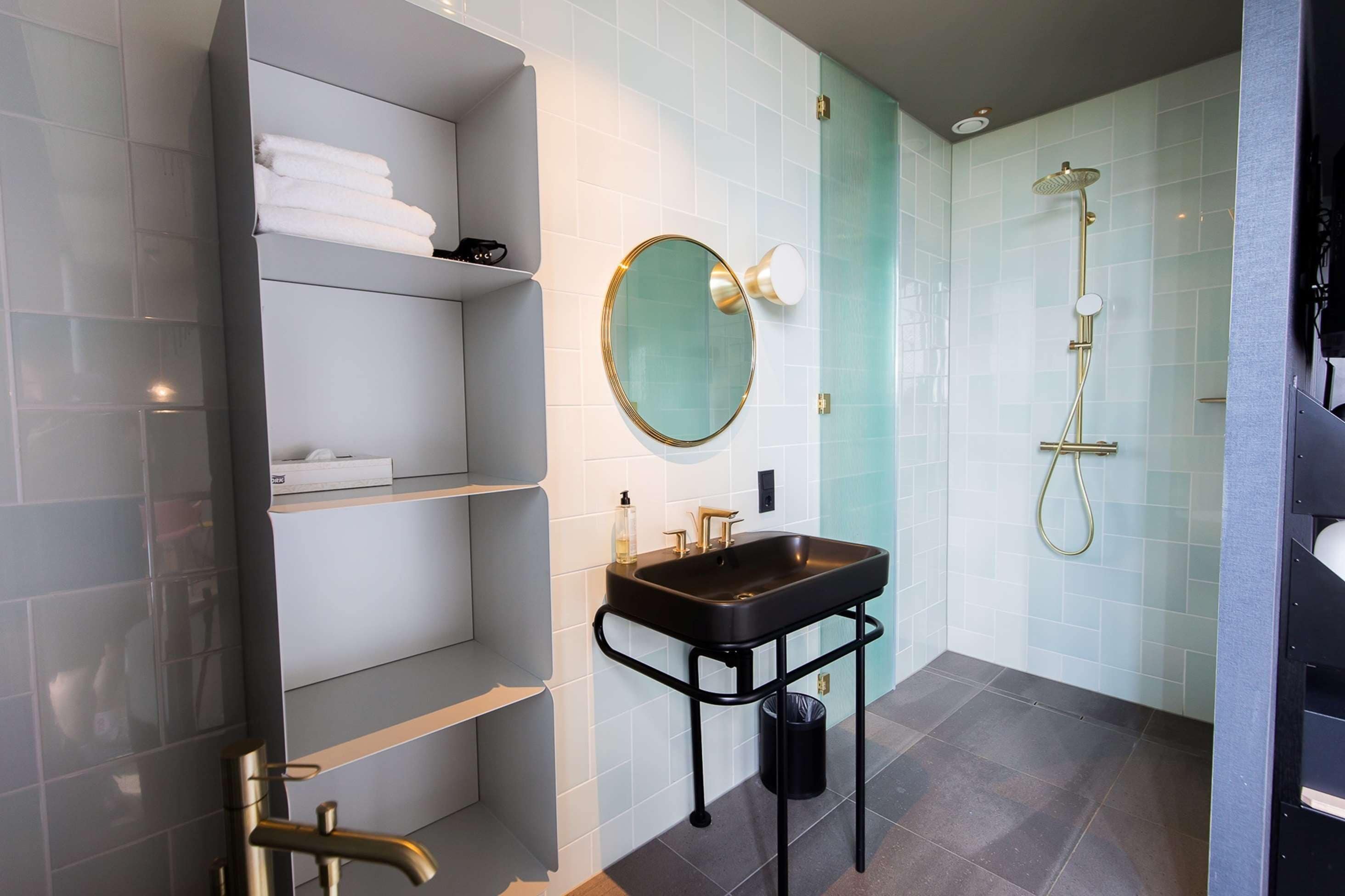A modern bathroom with a black sink, a round mirror, and a shower.