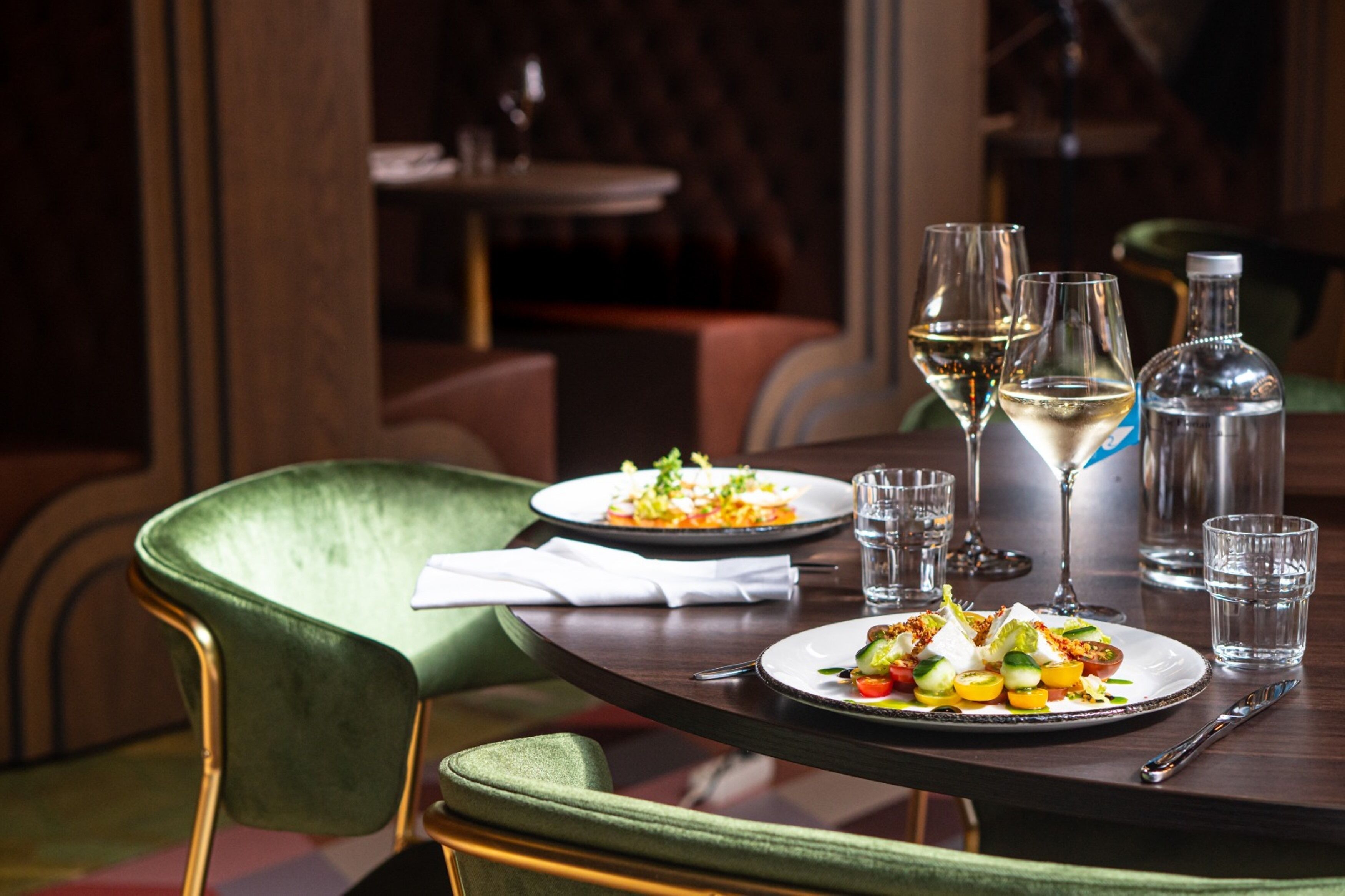 A dining table with two plates of food, three glasses, and a bottle.