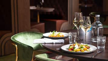 A dining table with two plates of food, three glasses, and a bottle.