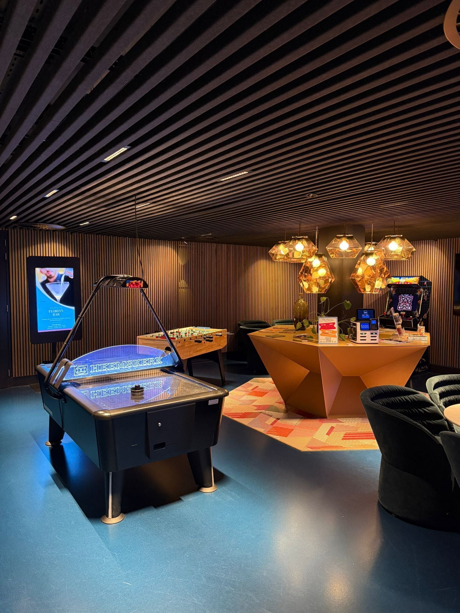 A modern indoor space with a foosball table, a bar area, and a seating area with a table and chairs.