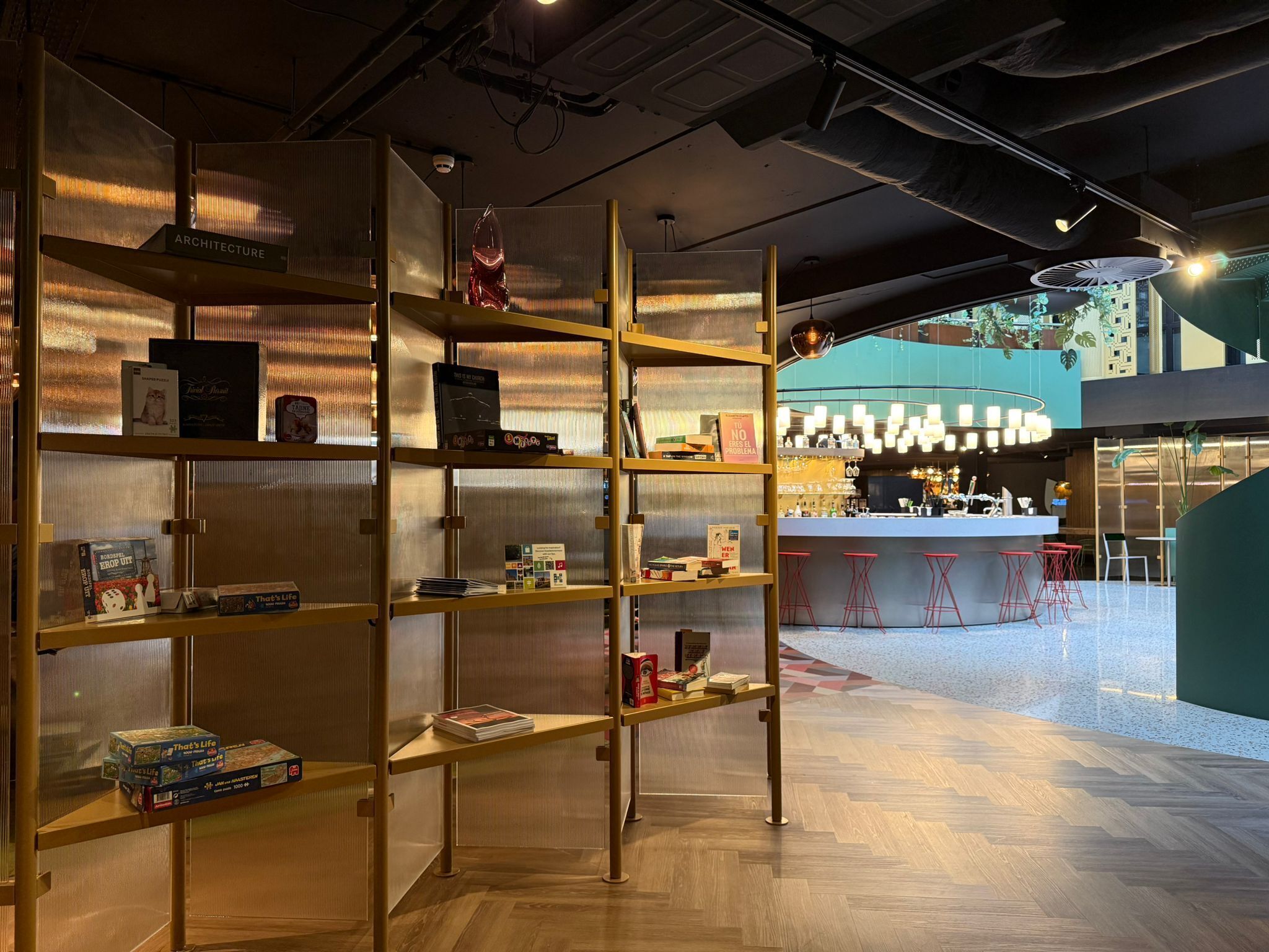 Ein modernes Interieur mit Holzbögen, die Bücher und Gesellschaftsspiele zeigen. Im Hintergrund ist eine Bar mit Hockern zu sehen.