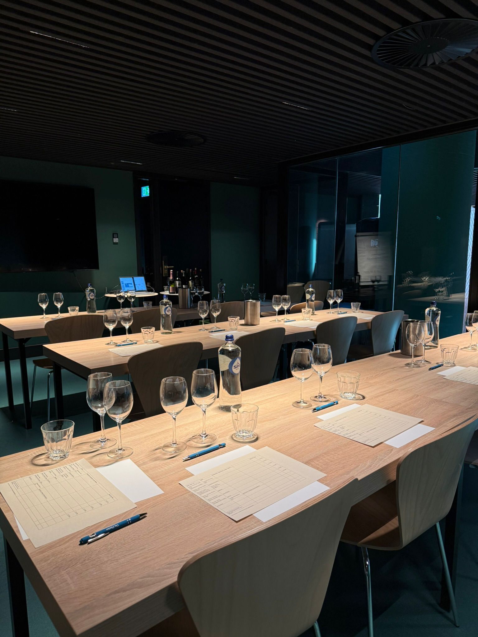 A conference room with long tables, chairs, and a large screen.