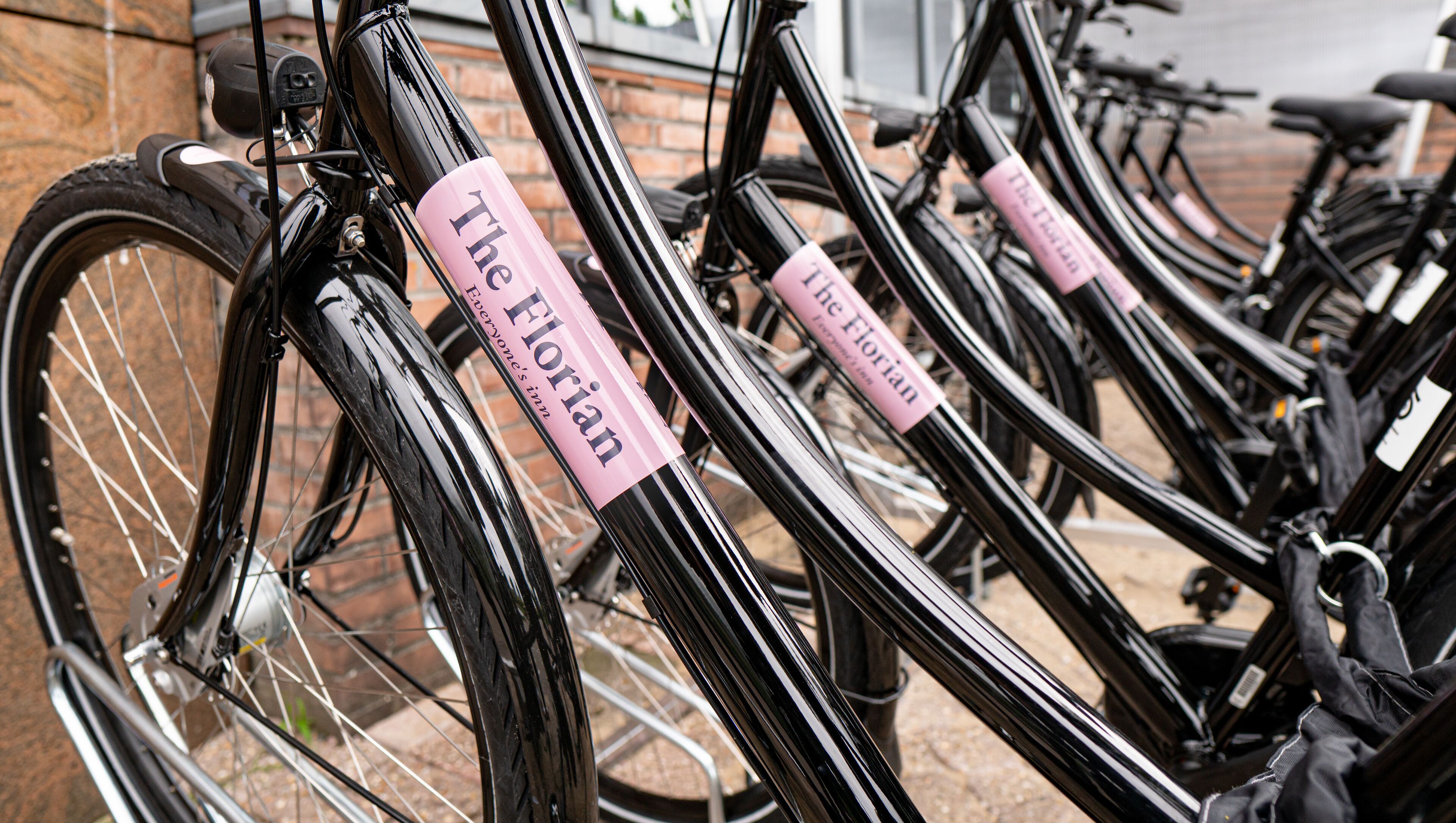 A row of bicycles with pink name tags, parked against a brick wall.