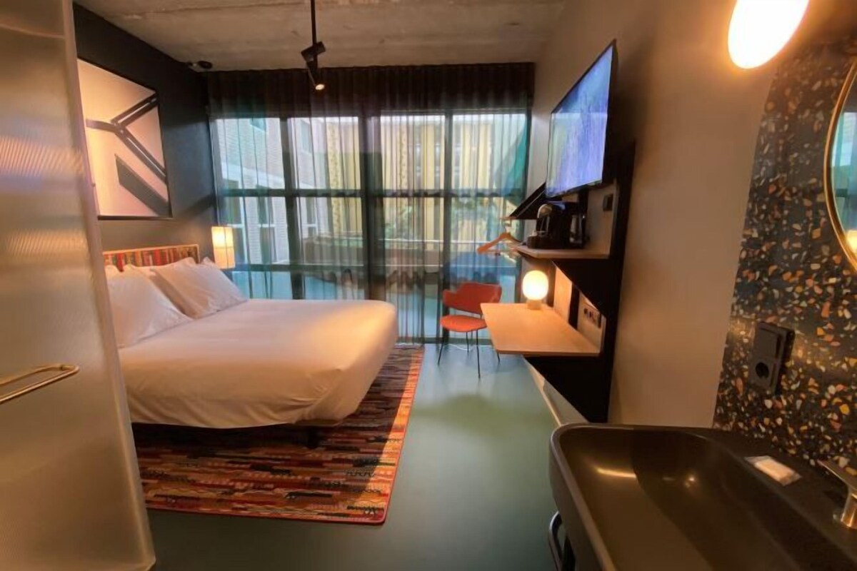 Una habitación de hotel con cama, escritorio, silla, televisor y baño.