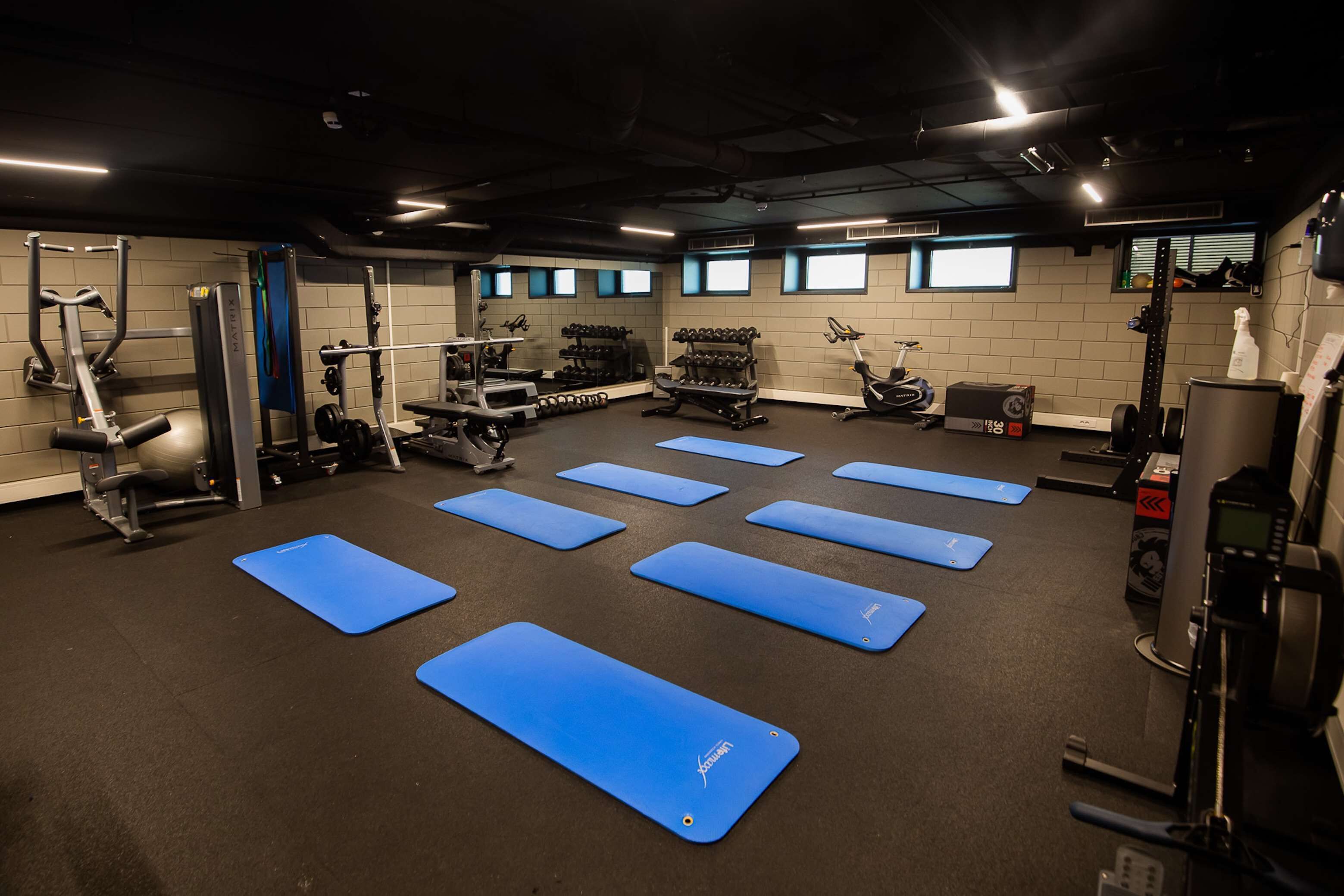 Une salle de sport équipée de divers appareils d’exercice, de tapis bleus et d’haltères.