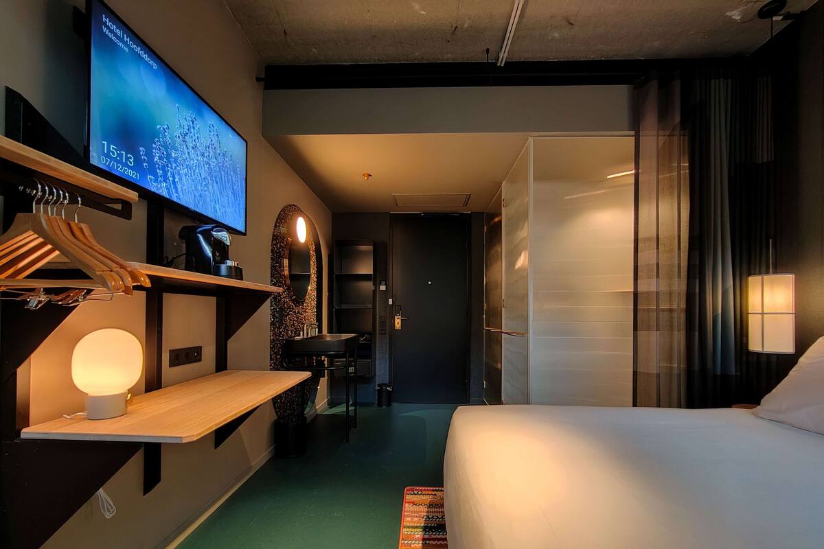 A hotel room with a bed, a desk with a lamp, a TV displaying a welcome message, and a bathroom with a mirror and sink.
