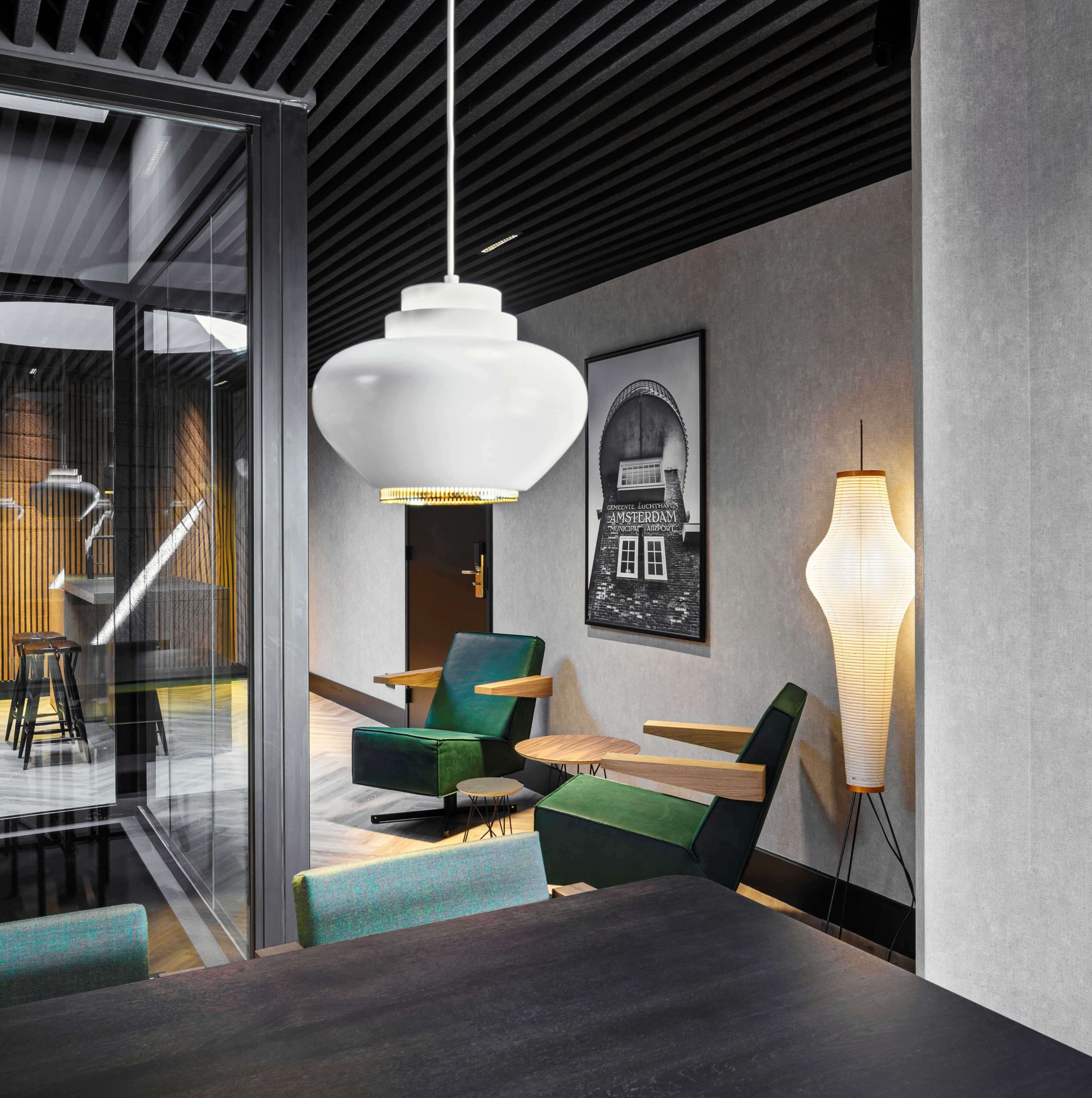 A modern interior with a glass partition, green upholstered chairs, a wooden table, and a hanging light fixture.