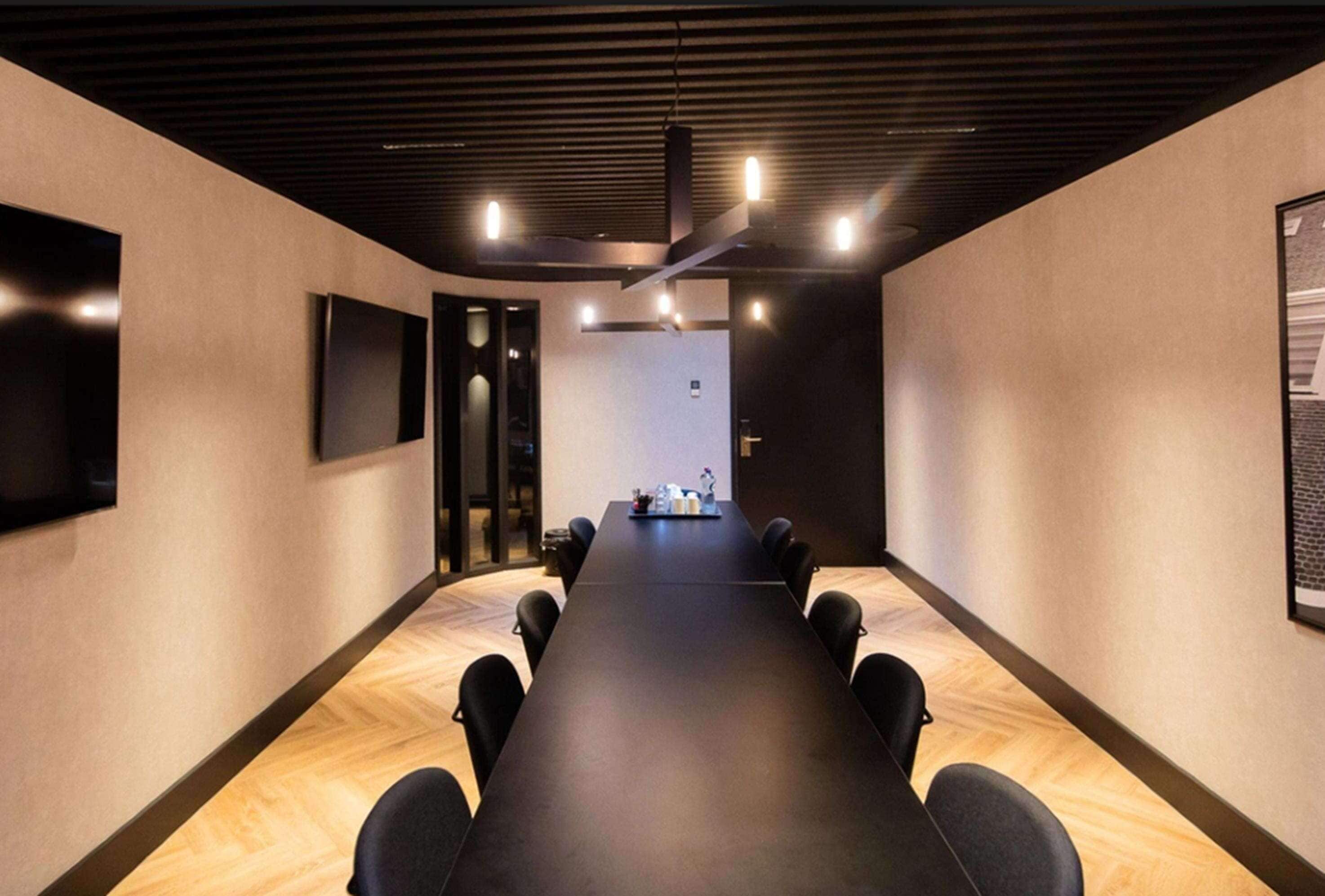 Une salle de conférence avec une longue table, des chaises, un téléviseur fixé au mur et une porte donnant sur une autre pièce.