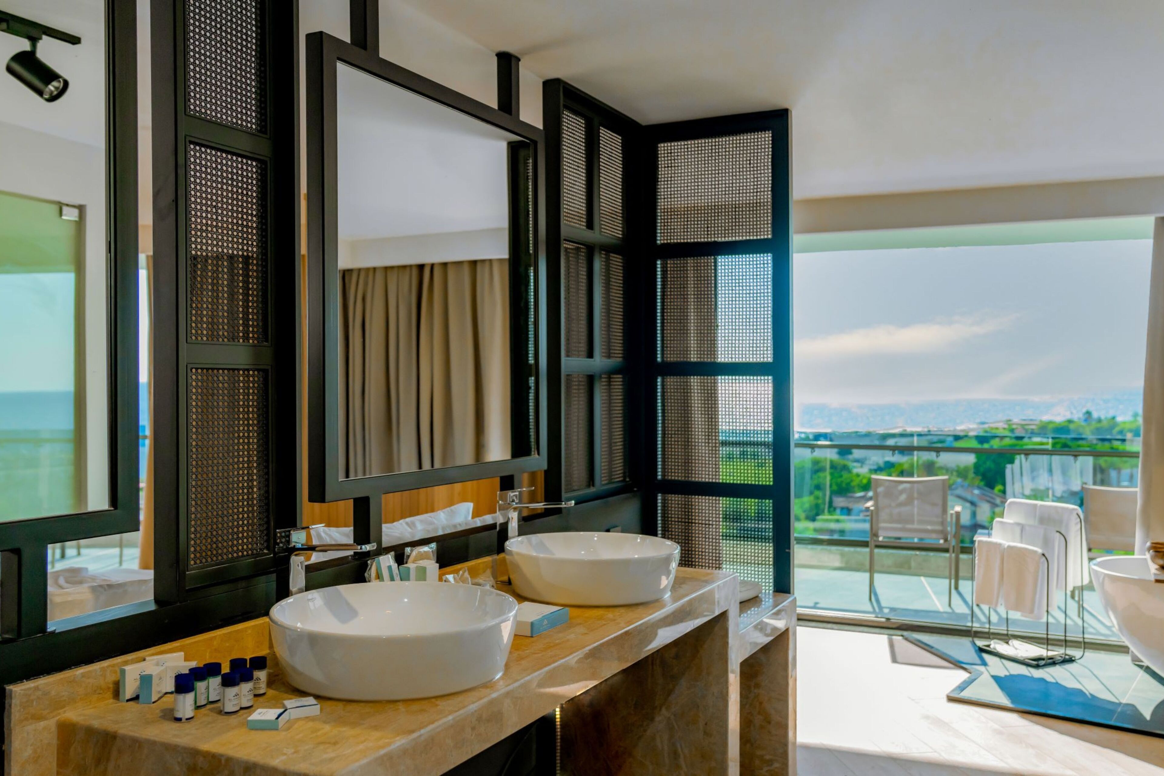 Un baño moderno con dos lavamanos grandes, un espejo amplio y vistas a un paisaje urbano a través de un ventanal.