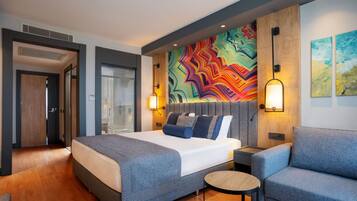 Una habitación de hotel moderna con una cama grande, una mesita redonda y una obra de arte abstracta y colorida en la pared.
