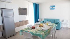 A modern kitchen with a refrigerator, dining table with chairs, and a blue sofa. - Villa Sabbie D'oro (Cava D'aliga)